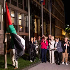 Slovenska beslutsfattare står framför landets parlamentsbyggnad och tittar på när Palestinas flagga hissas upp i en flaggstång.