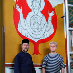 Piispa Arseni ja Jyrki Pouta maalaamansa seinämaalauksen edessä. Maalauksessa palava pensas.