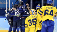 Ruotsin maalivahti Magnus Hellberg ja puolustaja Jonathan Pudas ihmettelevät maaliin mennyttä kiekkoa. Taustalla Suomen pelaajat juhlivat täysosumaa halaillen toisiaan.