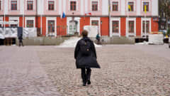 Pitkään tuulitakkiin ja pitkiin housuin pukeutunut nuorukainen kävelee mukulakivetystä Tarton kaupungin raatihuoneen torilla.