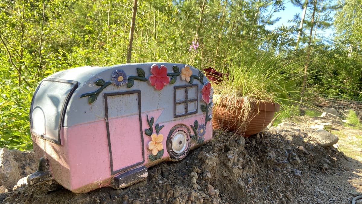 Kuvassa on Juupavaaran camping-alueelle asettuneen karavaanarinaisten pihalla oleva vaalenpunainen kukkaruukku, joka on matkailuvaunun näköinen