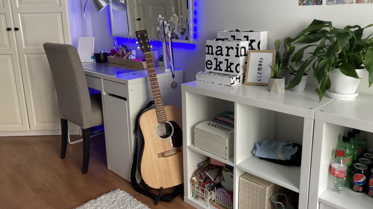 Kuvassa näkyy nuoren huone, jossa on esimerkiksi koulupöytä, akustinen kitara ja hyllykkö.