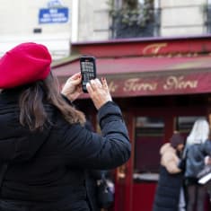 Punabaskerinen nainen ottaa kuvaa älypuhelimella kahvilasta.