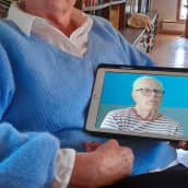 Nainen pitää kädessään tablettia, jolla näkyy hänen miehensä kuva.