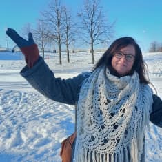 Kätensä sivuille levittänyt nainen seisoo talvisen Joensuun Laulurinteen edessä.