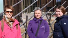 Kolme naista seisoo ulkosalla, taustalla koristeaita ja kulttuurikeskus.