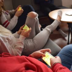 Ungdomar sitter med mobiler i handen.