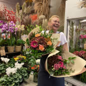 Iloinen kukkakauppias, jolla on kädessään kaksi kukkakimppua 