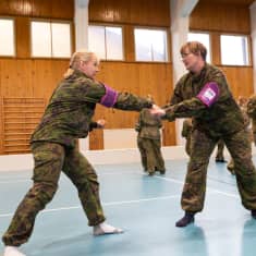 Maastopukuiset naiset harjoittelevat itsepuolustusotteita liikuntasalissa.