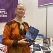 Kirjailija Kirsi Máret Paltto esittelee esikoisteostaan. Paltolla on päällään oranssi saamenpuku.