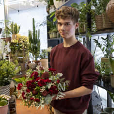 floristiopiskelija Kalle Huuhka pitelee tekemäänsä kukkakimppua käsissään kukkakaupassa.