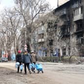 Ihmiset kantavat tyhjiä vesikanistereita tuhoutuneen kerrostalon vieressä.