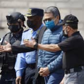 Viranomaiset saattavat Hondurasin entistä presidenttiä  Juan Orlando Hernandezia, jolla on kasvoillaan kasvomas.