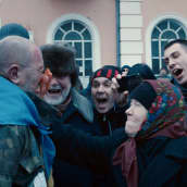 Joukko ihmisiä huutaa Ukrainan lippua harteillaan kantavalle miehelle. Vanha nainen työntää jotain punaista miehen kasvoille.