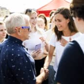 Sanna Marin kättelee aurinkolasipäistä ihmistä ja pitää kättää rintansa päällä. Ympärillä on ihmisiä.