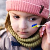 Pienen lapsen poskeen maalataan Ukrainan lippua.