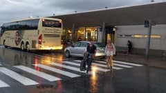 En buss står utanför Vasa flygplats. Två personer med resväskor går över vägen. Det är blött på marken.