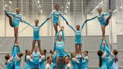 Kouluikäisten tyttöjen cheerleading-joukkue on tehnyt kuvassa pyramidin. Joukkueen jäsenillä on päällään yhtenevät sini-valkeat kisa-asut.