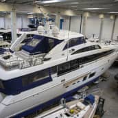 32 metriä pitkä, sinivalkoinen huvivene talvisäilössä hallissa, jossa on paljon muitakin veneitä.