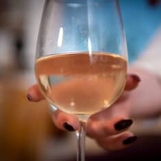 Nainen ottaa käteensä valkoviinilasin.