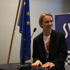 Akseli Tiitta hymyilee ja pitää puhetta SYL:n liittokokouksessa.