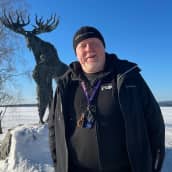 Mies seisoo lumisessa maisemassa patsaan edessä.