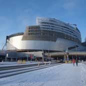 Tampereen Kannen Areena aka Nokia Arena kuvattuna 27.1.2021 auringonpaisteessa. Maa on lumessa ja kaksi kameraa kohti kävelevää ulkoilijaa näyttää pikkuruisilta suuren rakennuksen rinnalla.