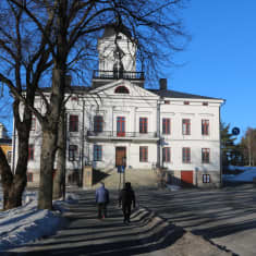 Två fotgängare går mot en vit byggnad.
