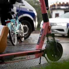 Kaksi poliisiautoa, joiden edustalla on skuutti ja ihmisiä.