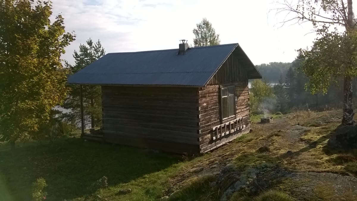Pieni hirsimökki, jonka taustalla häämöttää Laatokka Venäjän Karjalan Lumivaaralla. 