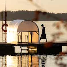 Two people walking on a dock at sunrise, with golden sunshine reflecting on the water.