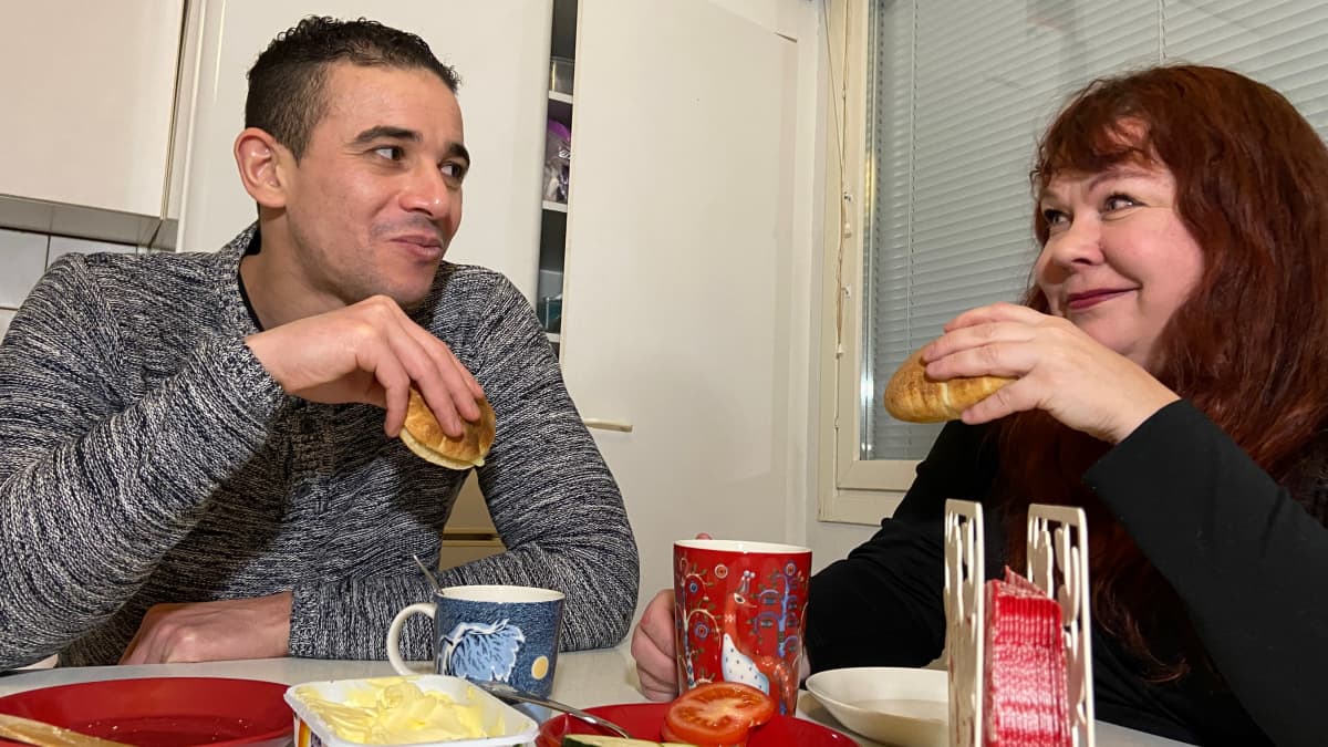 Algerialainen maahanmuuttajamies ja hänen suomalainen pitkätukkainen vaimonsa katsovat toisiaan keittiön pöydän ääressä ja syövät miehen leipomaa pita-leipää