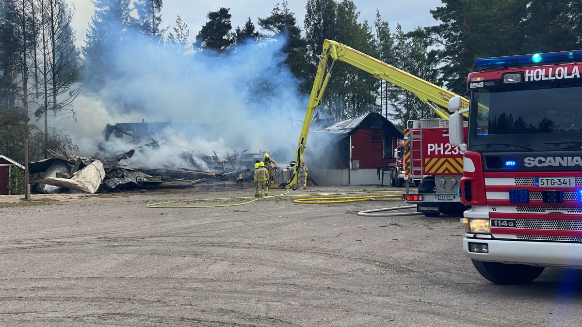 Kaksi pelastuslaitoksen sammutusykiskköä ja muutama palomies sammuttaa paloa Orimattilan Virenojalla. Taustalla maan tasalle palanut rakennus savuaa harmaana.