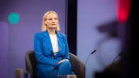 A blonde middle-aged woman in a light-blue suit sits in a TV studio.