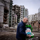 Mies kävelee tarvikkeiden kanssa pommituksissa tuhoutuneiden talojen ohitse.