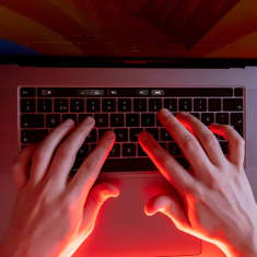 Punaisessa valossa kädet kannettavan tietokoneen näppäimistöllä.