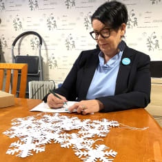 Nainen kirjoittaa lumihiutaleen muotoisille lapuille lasten lahjatoiveita.