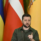 Ukrainan presidentti puhuu taustallaan lippuja.