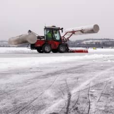 Pieni traktoriaura Jyväsjärven jäällä tekemässä retkiluistelurataa. Luistelija katsoo auraa radan sivusta.