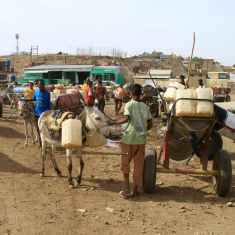 Aasit kuljettavat vettä kärryillä mutaisessa maastossa Sudanissa.