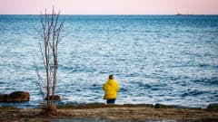 Nainen rannalla keltaisessa toppatakissa katselee kohti horisonttia.