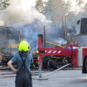 Hiittenharjun hotelli palaa Harjavallassa 14.7.2021, palomies katselee tilannetta paitahihasillaan helteisenä iltana, kuvassa myös paloauto. Savu kohoaa.