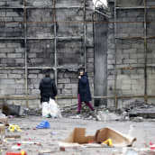 Kaksi henkilöä kävelee tuhoutuneen rakennuksen vieressä.