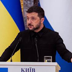 Volodymyr Zelenskyi puhuu lehdistötilaisuudessa Ukrainan lipun edessä.