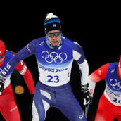 Joni Mäki hiihtää sinisessä asussa, takanaan kaksi punaiseen asuun pukeutunutta hiihtäjää.
