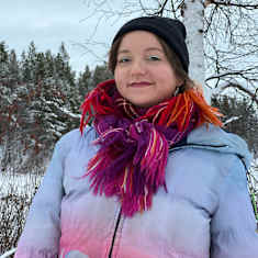 Sunna Nousuniemi hymyilee Inarijärven rannalla, lumisessa koivikossa, pipo päässä, saamen huivi kaulassa 15.1.2025 Inarissa.