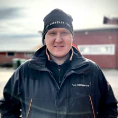 Sikatilan isäntä Antti Hyppönen katsoo kameraan mustassa takissa ja pipossa.