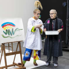 Kemin kaupunginteatterin näyttelijät Johanna Virsunen ja Satu Tala esittelevät värien maailmaa. Vieressä maalausteline, johon on vedetty monenvärisiä kaaria.