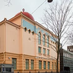 Gatuvy över Helsingfors synagoga - ett gult hus i klassisk stil, ett rött kupoltak skymtas där ett tak ska vara.