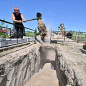 Työntekijä lapioi hiekkaa hautaan.